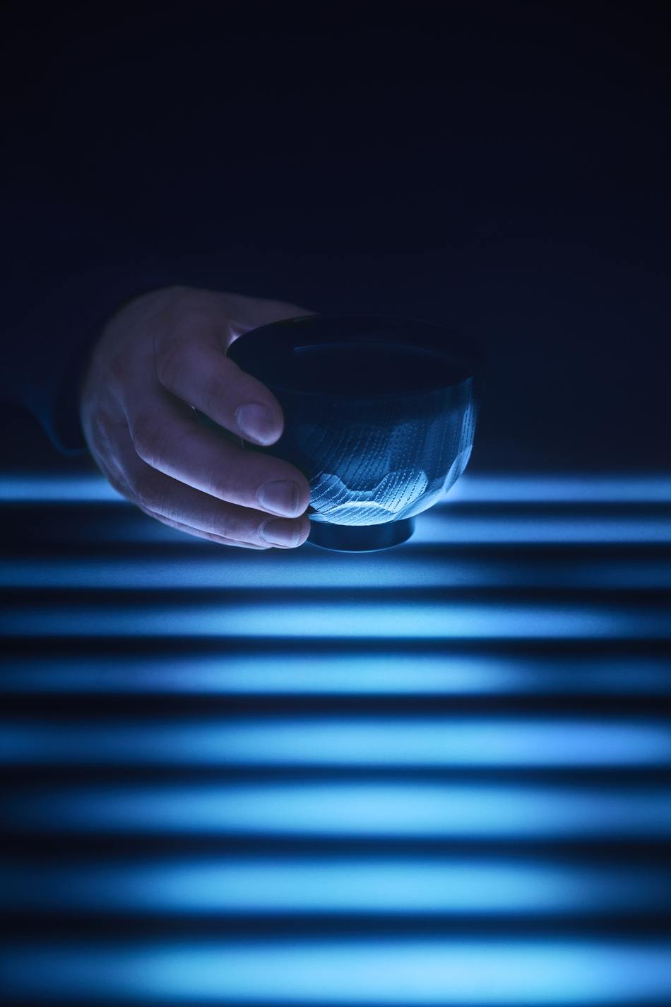 A hand lifting a bowl from the glowing acrylic surface of the Tabula Rasa table